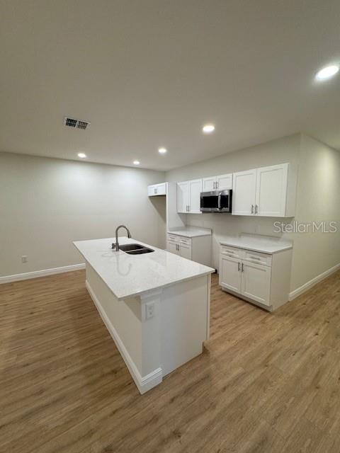 kitchen featuring sink, light hardwood / wood-style flooring, white cabinetry, light stone counters, and an island with sink