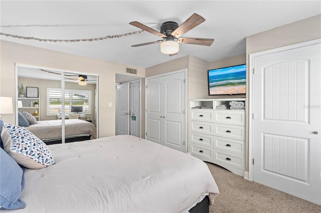 bedroom featuring ceiling fan, visible vents, carpet floors, and multiple closets