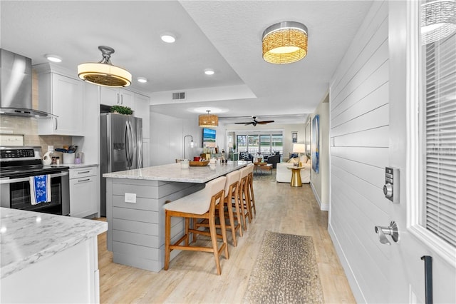 kitchen featuring a breakfast bar, open floor plan, stainless steel appliances, light wood-style floors, and wall chimney range hood