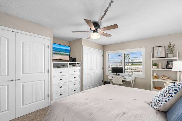 bedroom featuring a ceiling fan, two closets, carpet flooring, and a textured ceiling