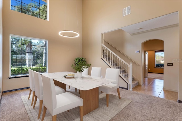 dining space featuring visible vents, arched walkways, light colored carpet, stairs, and a high ceiling