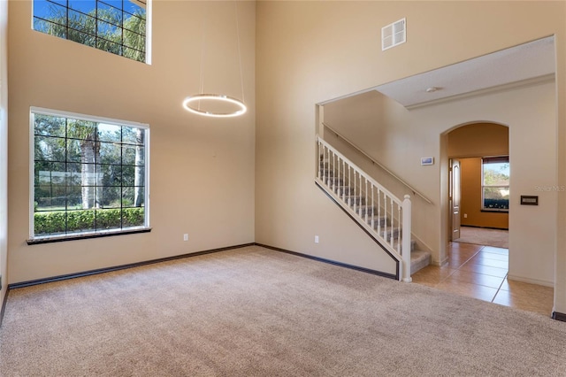 carpeted spare room featuring a wealth of natural light, arched walkways, visible vents, and a high ceiling