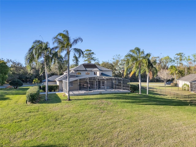 rear view of house featuring glass enclosure, fence, and a yard