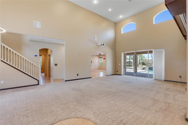 unfurnished living room featuring arched walkways, visible vents, carpet, and stairs