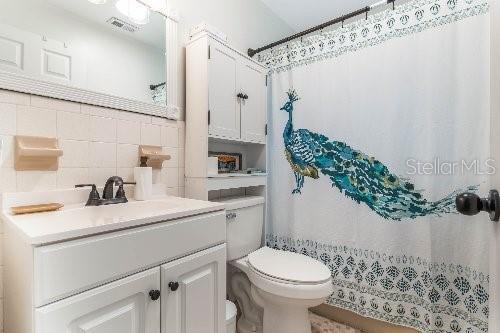 bathroom with tile walls, a shower with shower curtain, vanity, tasteful backsplash, and toilet