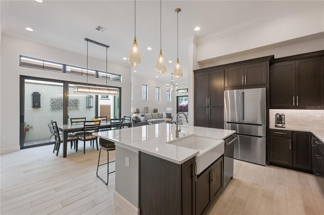 kitchen with sink, appliances with stainless steel finishes, backsplash, an island with sink, and decorative light fixtures