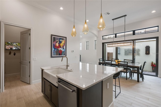 kitchen featuring sink, dishwasher, an island with sink, pendant lighting, and light stone countertops