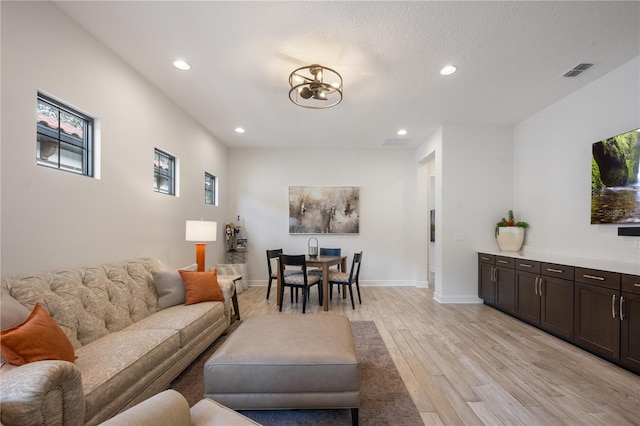 living room with a chandelier, light hardwood / wood-style flooring, and a textured ceiling