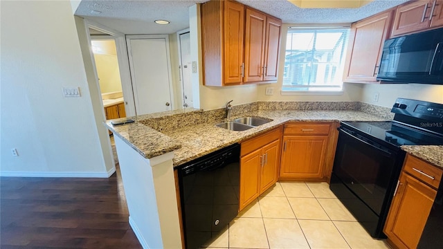 kitchen featuring black appliances, sink, kitchen peninsula, light stone countertops, and a textured ceiling