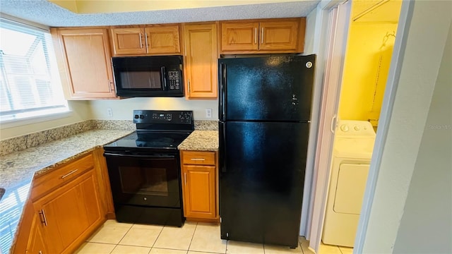 kitchen with washer / clothes dryer, light stone countertops, light tile patterned floors, and black appliances