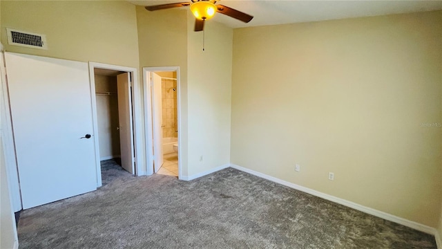 unfurnished bedroom featuring a spacious closet, ceiling fan, dark carpet, ensuite bath, and a closet