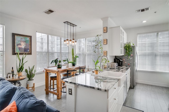 kitchen featuring white cabinetry, decorative light fixtures, light stone countertops, and crown molding