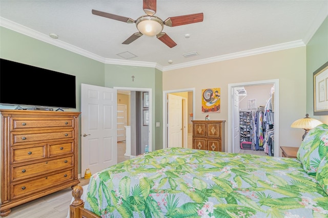 bedroom with light wood finished floors, a walk in closet, visible vents, and crown molding