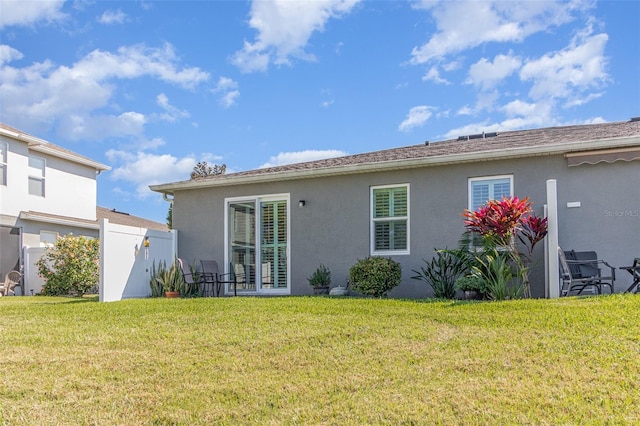 back of house featuring a lawn, fence, and stucco siding