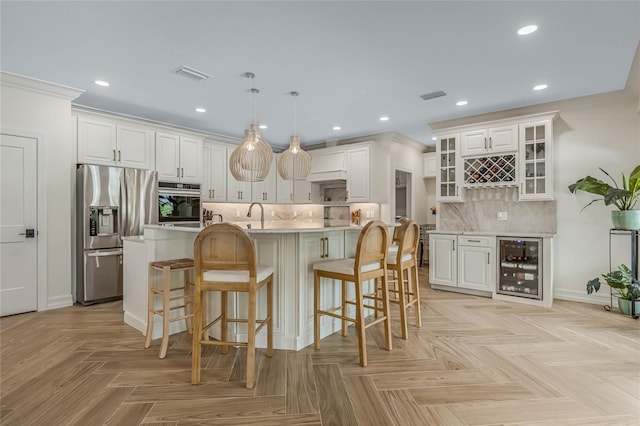 kitchen with beverage cooler, appliances with stainless steel finishes, decorative light fixtures, and a center island with sink