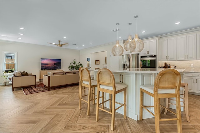 kitchen featuring a breakfast bar, white cabinetry, hanging light fixtures, stainless steel appliances, and light parquet floors