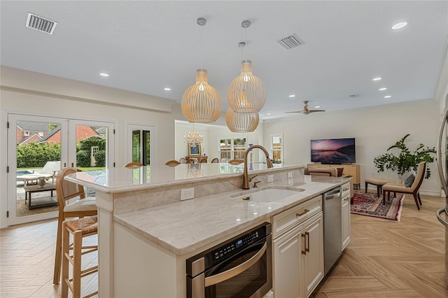 kitchen with sink, light parquet floors, a kitchen breakfast bar, light stone countertops, and a center island with sink