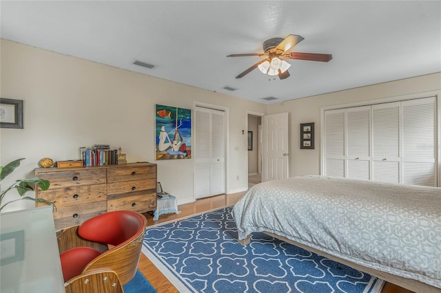 bedroom with ceiling fan, wood-type flooring, and multiple closets