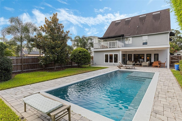 rear view of property featuring an outdoor living space, a balcony, a fenced in pool, and a patio area