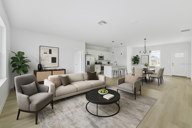living room featuring light wood-style floors, baseboards, a chandelier, and visible vents