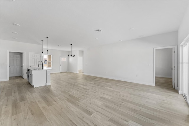 unfurnished living room with baseboards, visible vents, a sink, and light wood-type flooring