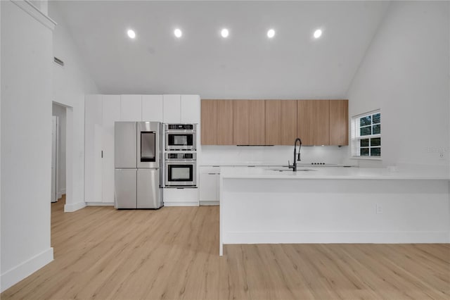 kitchen featuring high vaulted ceiling, a sink, stainless steel appliances, light countertops, and modern cabinets