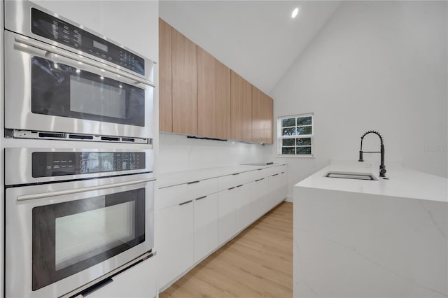 kitchen with modern cabinets, light wood-style flooring, a sink, stainless steel double oven, and light stone countertops