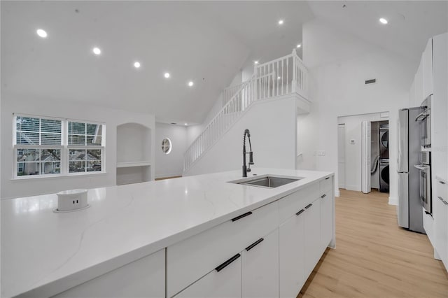 kitchen with a sink, white cabinetry, light wood finished floors, stacked washer / dryer, and light stone countertops