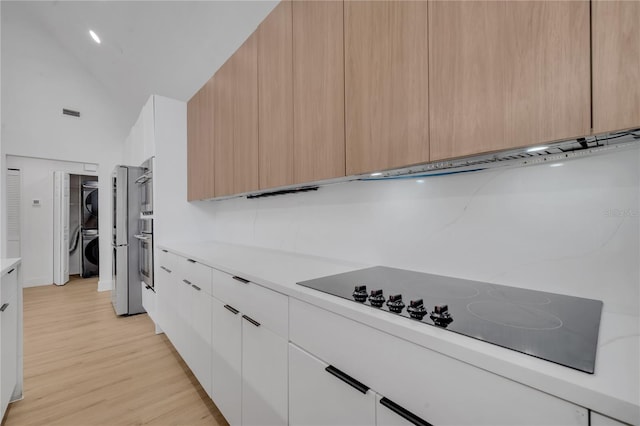 kitchen with stacked washer / dryer, light countertops, light wood-type flooring, modern cabinets, and black electric cooktop