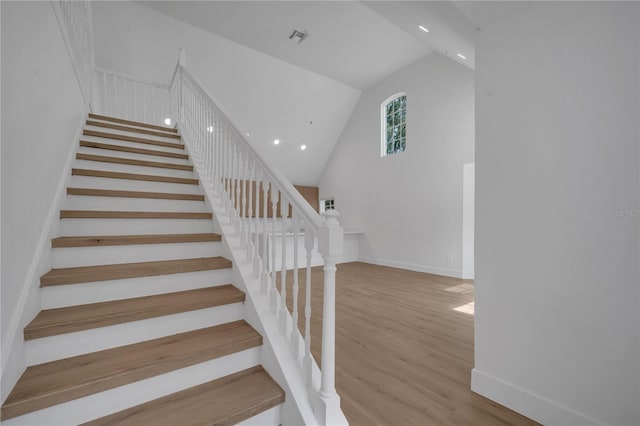 stairway featuring wood finished floors, visible vents, baseboards, high vaulted ceiling, and recessed lighting