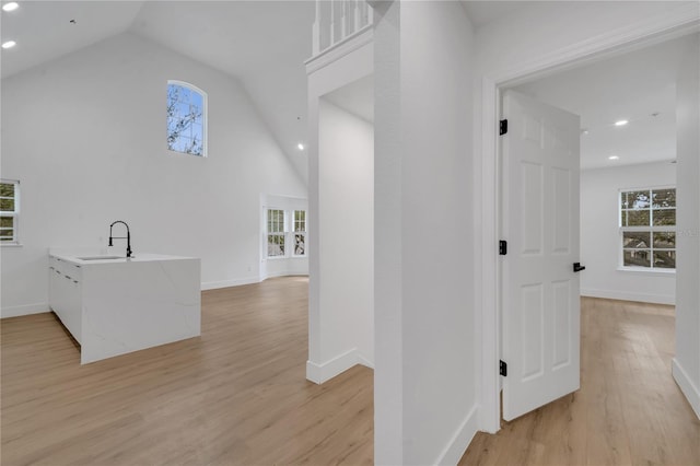 hallway featuring a wealth of natural light, vaulted ceiling, light wood-type flooring, and a sink