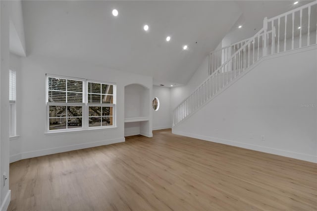 unfurnished living room with stairway, wood finished floors, baseboards, high vaulted ceiling, and arched walkways