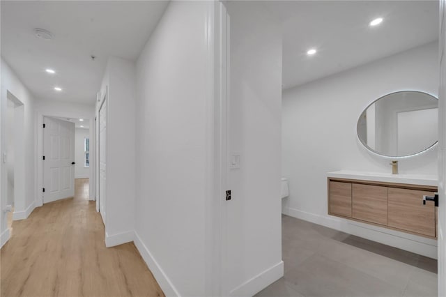 hallway with recessed lighting, baseboards, and a sink