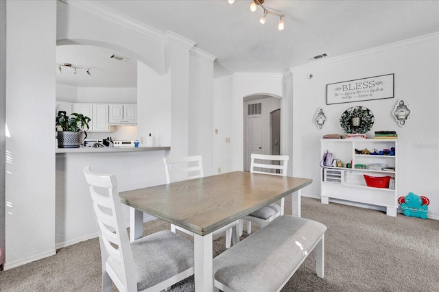 carpeted dining room with track lighting and ornamental molding