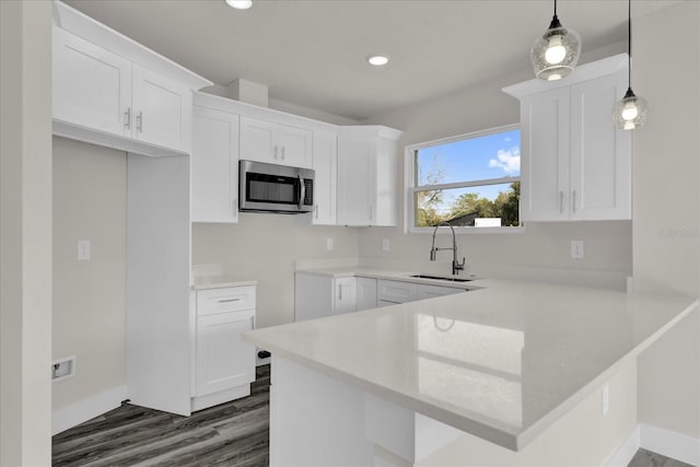 kitchen with white cabinetry, kitchen peninsula, decorative light fixtures, sink, and dark wood-type flooring