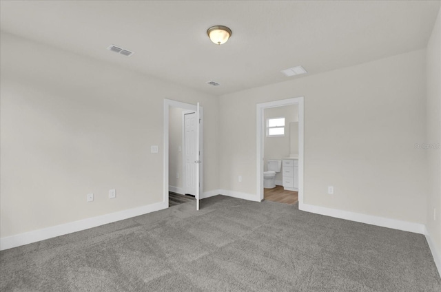 unfurnished bedroom with dark colored carpet and ensuite bathroom