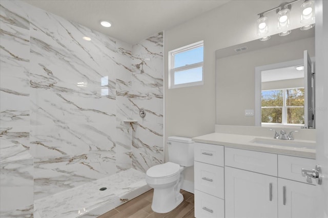 bathroom with vanity, tiled shower, toilet, and a wealth of natural light