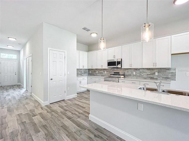 kitchen featuring white cabinetry, stainless steel appliances, hanging light fixtures, and light stone counters