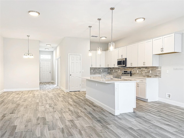 kitchen featuring appliances with stainless steel finishes, an island with sink, pendant lighting, decorative backsplash, and white cabinets