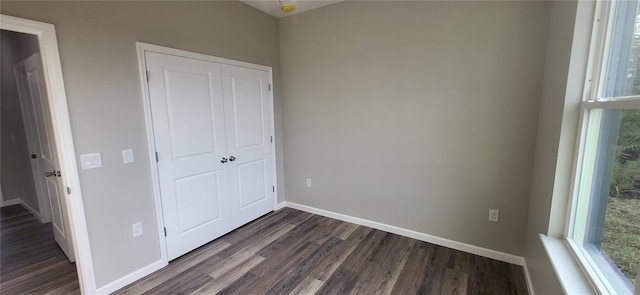 unfurnished bedroom with multiple windows, dark wood-type flooring, and a closet