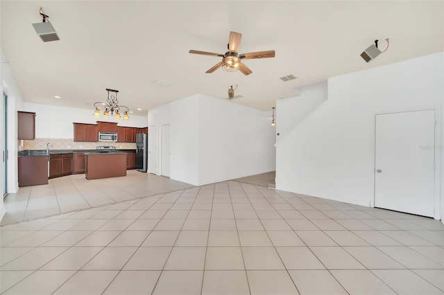 unfurnished living room with sink, ceiling fan with notable chandelier, and light tile patterned floors