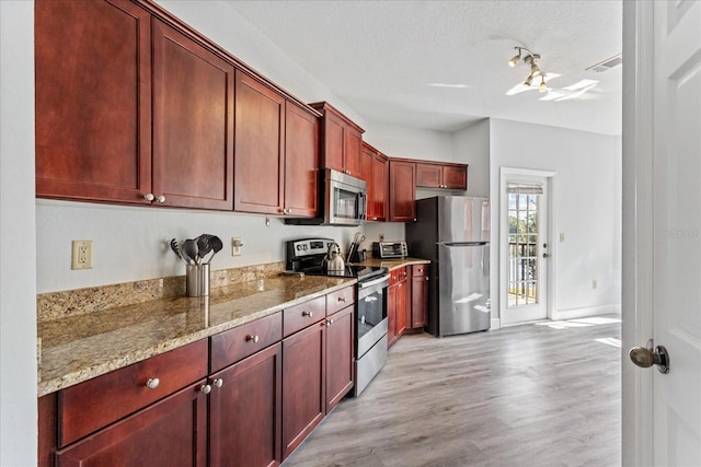 kitchen featuring stainless steel appliances, light wood-type flooring, a textured ceiling, and light stone counters