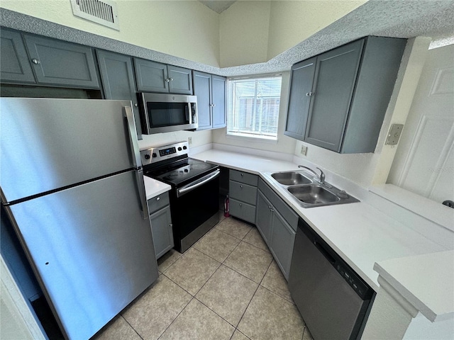 kitchen featuring stainless steel appliances, sink, light tile patterned floors, and gray cabinets