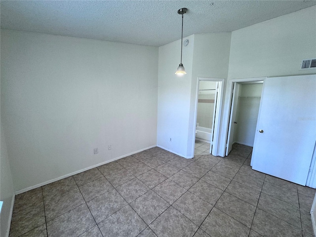 unfurnished bedroom featuring a closet, ensuite bath, tile patterned flooring, and a textured ceiling