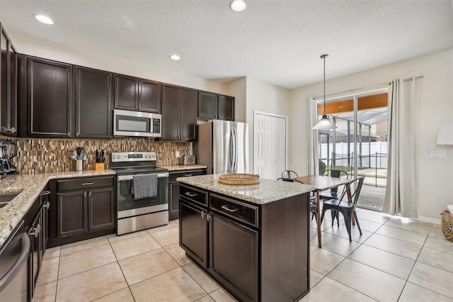 kitchen featuring dark brown cabinets, hanging light fixtures, appliances with stainless steel finishes, light stone countertops, and backsplash