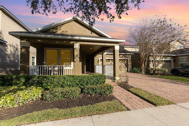 view of front facade featuring decorative driveway, covered porch, a garage, and stucco siding