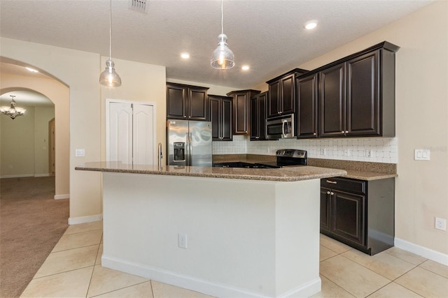 kitchen featuring dark brown cabinetry, decorative light fixtures, an island with sink, stainless steel appliances, and backsplash