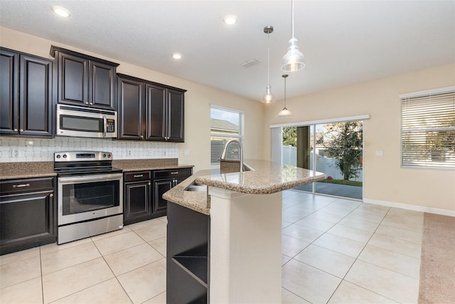 kitchen with tasteful backsplash, decorative light fixtures, a center island with sink, light tile patterned floors, and stainless steel appliances