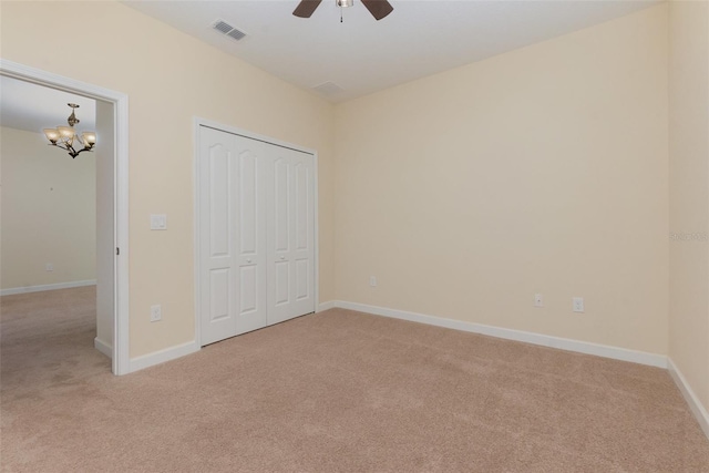 unfurnished bedroom with ceiling fan with notable chandelier, light colored carpet, and a closet