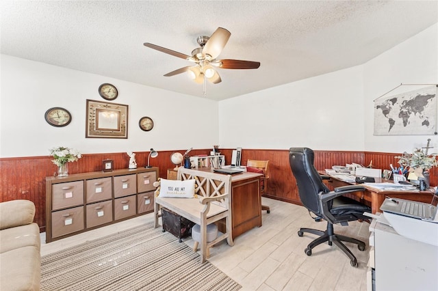 home office featuring ceiling fan, wooden walls, a textured ceiling, and light hardwood / wood-style flooring